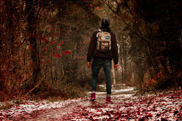 Muž v bundě s batohem na zádech jdoucí zimním lesem